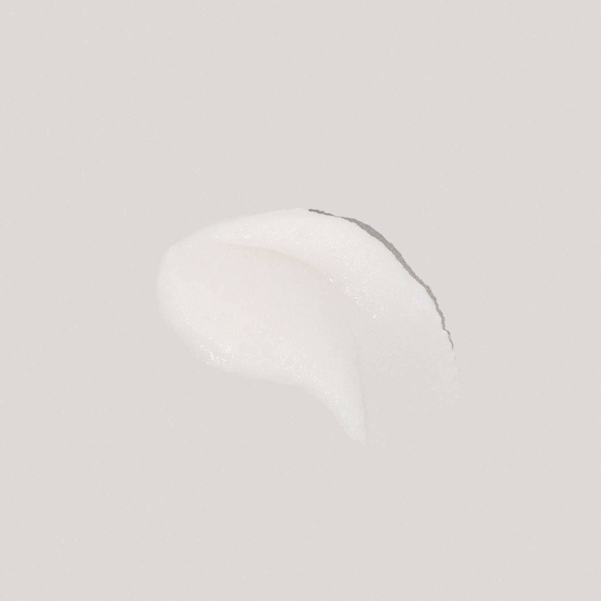 A dollop of creamy white body scrub, glistening slightly, set against a soft gray background.