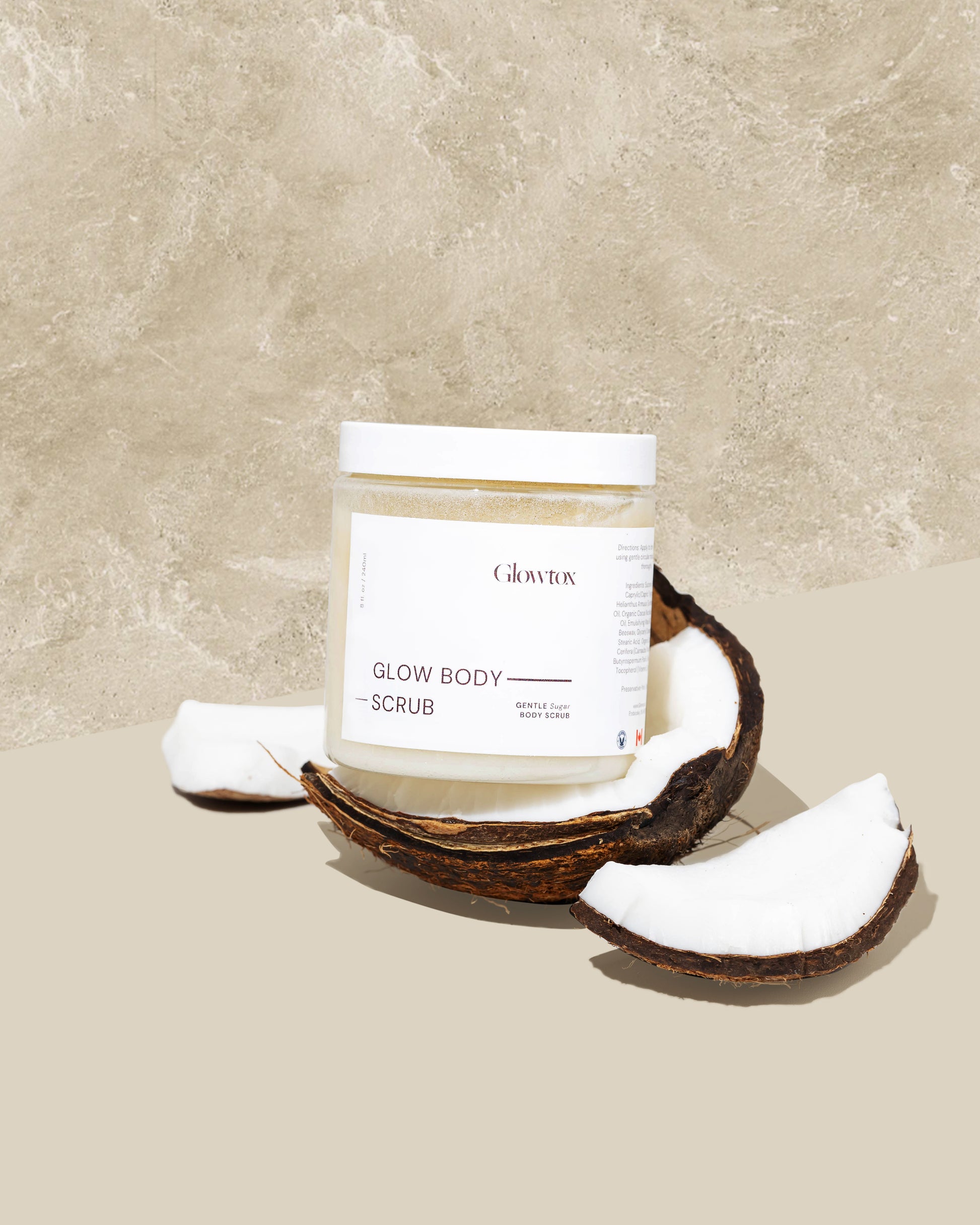 A jar of Glowtox Glow Body Scrub rests on a textured background, surrounded by coconut pieces, highlighting natural beauty skincare.
