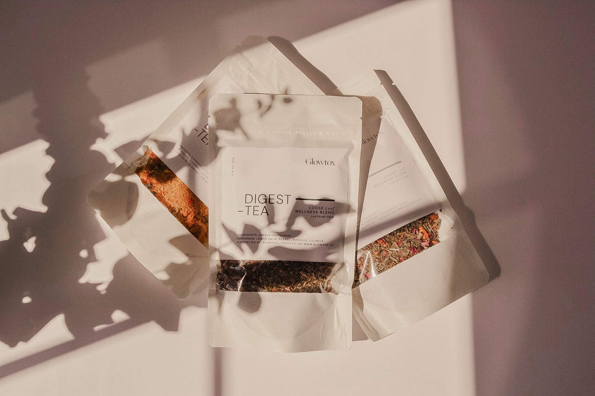 Three packets of herbal tea labeled "Digest Tea" arranged on a surface, with soft shadows and sunlight illuminating them.